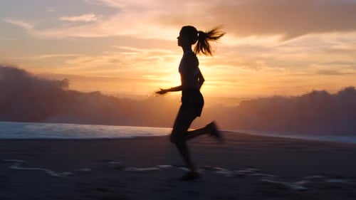 Active, fit female runner running alone at the beach during a beautiful sunset
