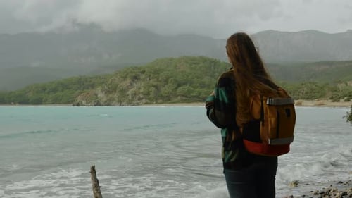 A girl travels with a backpack alone, overlooking the ocean. The woman breathes in the air on/