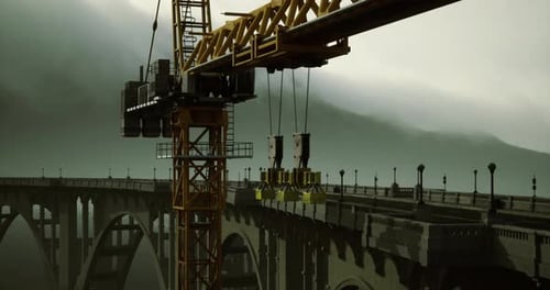 Una grúa de construcción opera sobre un puente en un brumoso paisaje montañoso