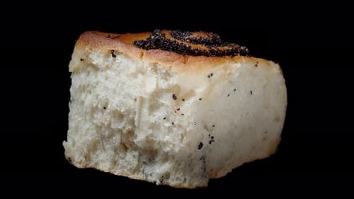 The bun with poppy seed filling rotates. Isolated on a black background side view. Close-up