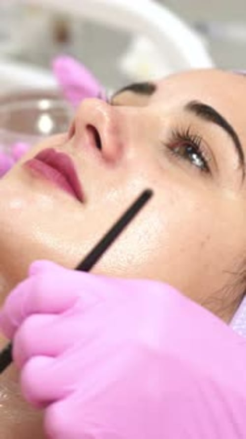 Beautician applying peeling on woman's face in spa. Face cosmetic procedure.