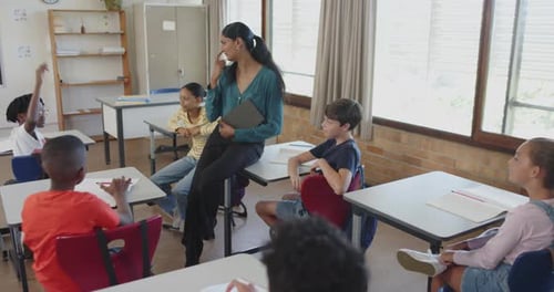 In school, teacher engaging with students raising hands in classroom discussion