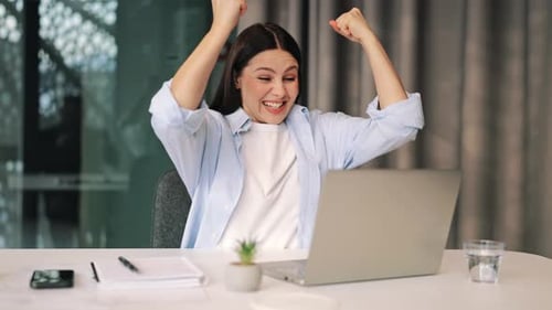 Excited Woman Celebrating Success in Workplace Using Laptop