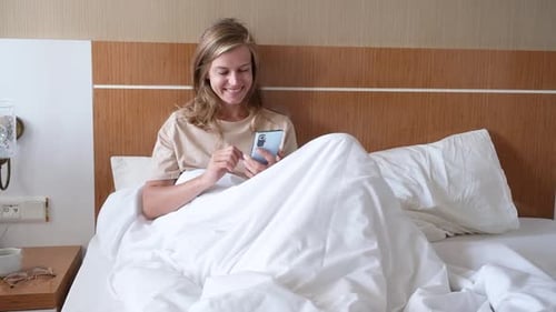 Young woman using smartphone in hotel bed