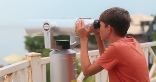 Boy Looks Through Seaside Binoculars on Balcony