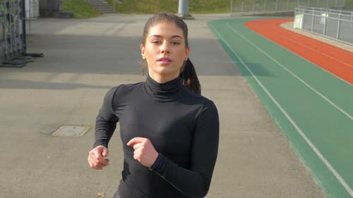 Young Woman Running At A Track And Field Stadium - medium shot