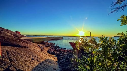 Hyperlapse-Aufnahme einer friedlichen felsigen Küste mit Meer und Steg bei goldenem Sonnenuntergang am Horizont - Anc