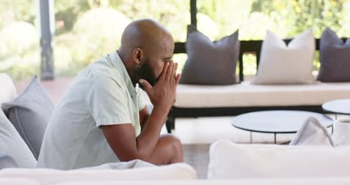 Thinking deeply, man sitting on sofa in living room, contemplating thoughts, copy space