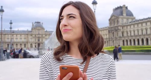Jovem feliz enviando uma mensagem de texto em seu celular em frente ao Louvre