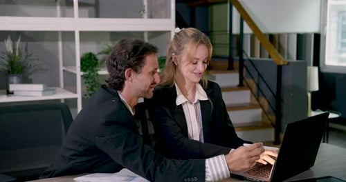 Businessman and businesswoman celebrating success while looking at laptop during office meeting