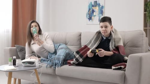 Boy Plays Video Games While Woman Uses Nebulizer