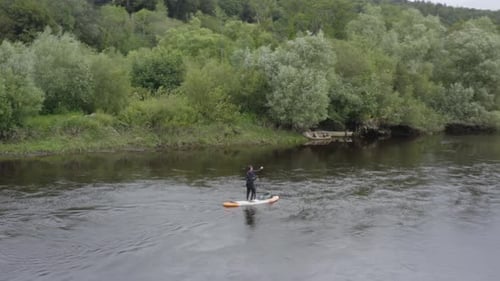 Aerial orbits lone male paddling stand up paddleboard on small river