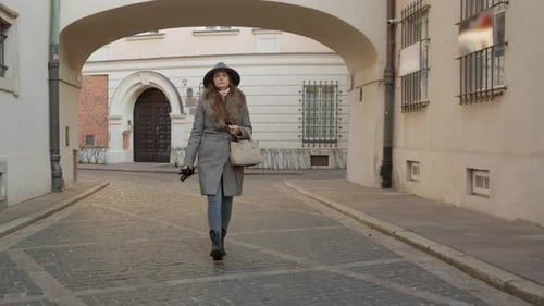 A woman walks through a historic archway on a cobblestone alley in Warsaw.