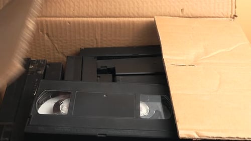 Hand Opens Box of Black VHS Tapes