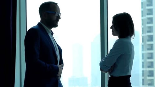 Young businesspeople chatting relaxed near window silhouette in modern office