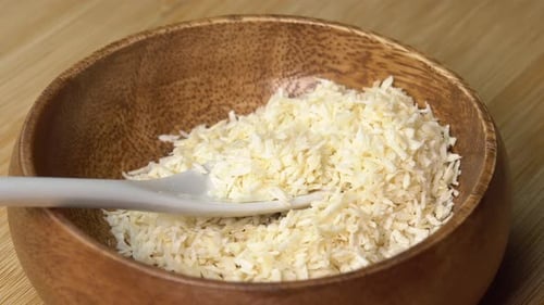 Floques de noix de coco dans un bol en bois avec cuillère rotative sur une planche de bois. Copeaux de noix de coco ou noix de coco râpée