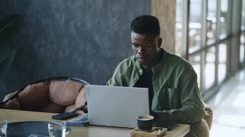 A Young African American Writer Sits at a Cafe Desk Deeply Absorbed in Thought As He Searches for