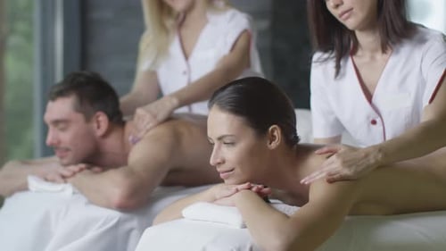 Young couple is getting a relaxing massage from female masseurs in wellness center.