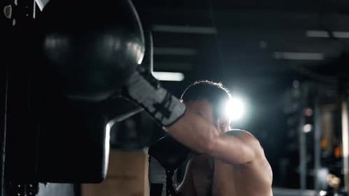 A Muscular Alone Boxer is Hits Punching Bag in the Gym