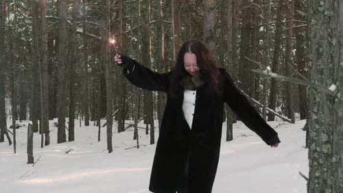 Mulher segurando faísca ardente com braços estendidos comemorando na floresta de inverno