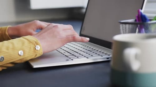 Midsection of woman sitting at desk using laptop with copy space at home, slow motion