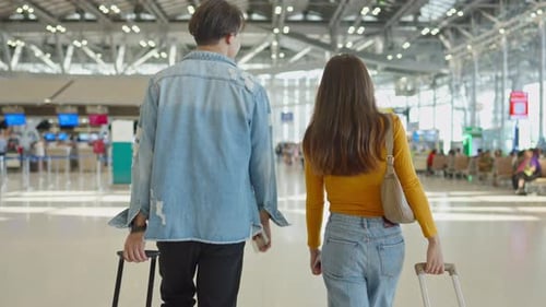 Rear view of young couple walking in airport terminal to boarding gate.