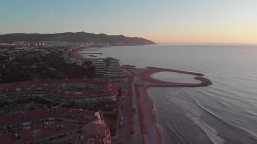 Drone flying over touristy city on coastline with mountain range standing on horizon and glowing in