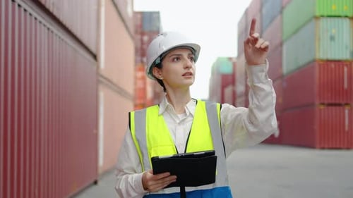 Skilled female caucasian engineer in a uniform and white hard hat checks work using a tablet.