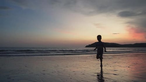 Little boy is running along a sand beach at sunset