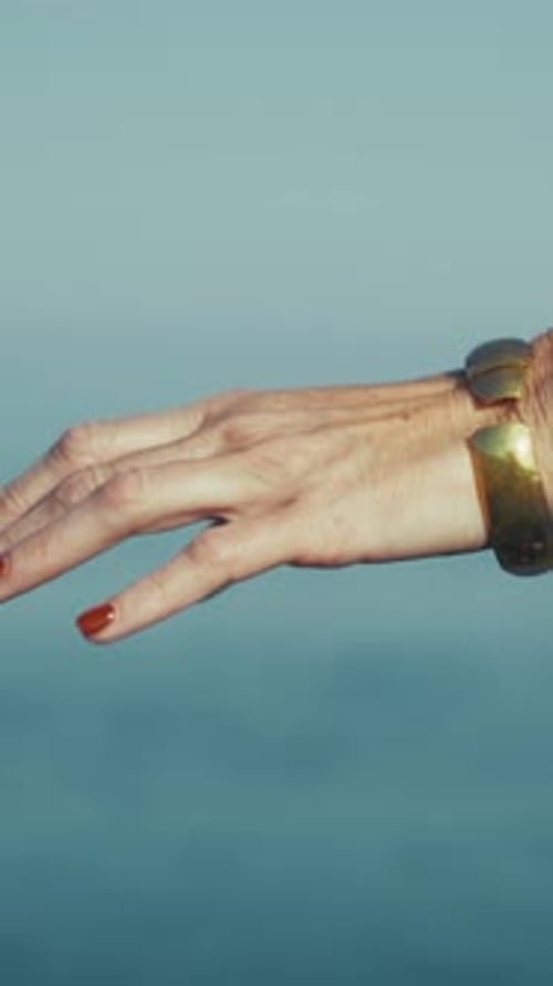 Hand Of A Woman With A Golden Bracelet With Blurrer Sea Background
