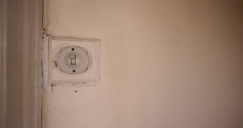 Finger Flicking an Old-fashioned Light Switch on Wall