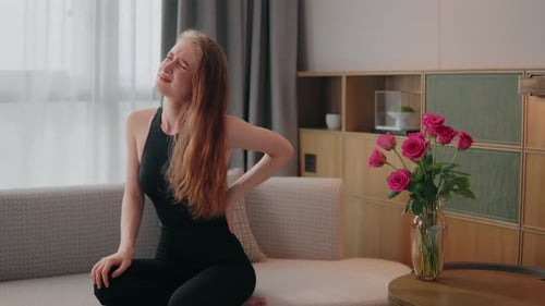 Young Woman on a Sofa Clutches Her Lower Back in Pain Painful Suffering From Injury Backache