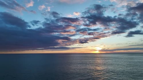 Aerial Video of Fiery Golden Sun Setting Over Ocean Horizon With Purple Clouds Above