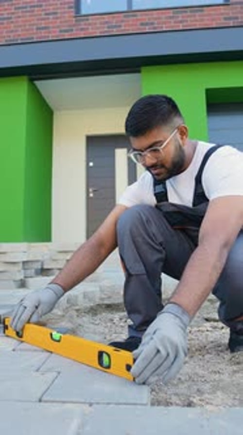 Indian Construction Worker Uses a Level Tool to Precisely Align Paving Stones During Installation