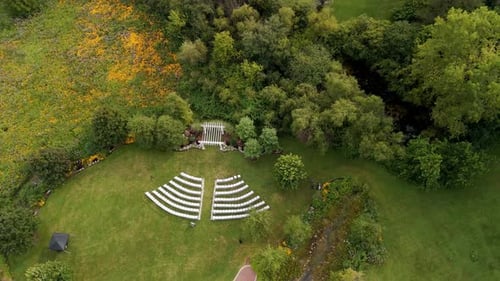 The Aerial Drone View of the Outdoor Wedding Setup with Rows of White Chairs Facing a Wooden Arch