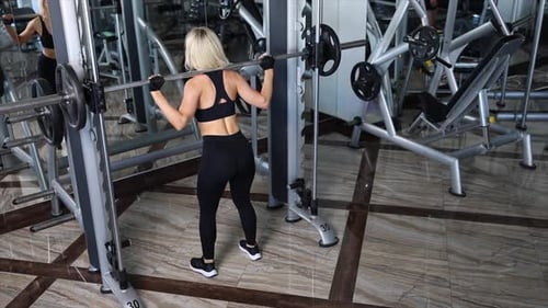 Athletic woman performing squats with barbell in gym