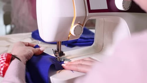 Woman sewing blue fabric with professional machine in workshop, closeup