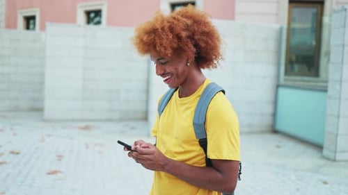 Young African-American student uses mobile phone while walking on university campus