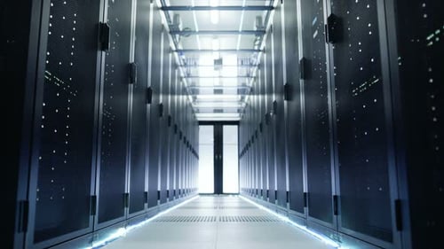 La caméra traverse un grand centre de données en activité avec des baies de serveurs et un plafond en verre.