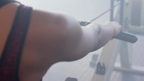 Midsection of african american woman training on rowing machine at gym, in slow motion