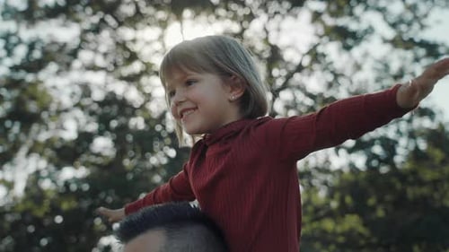 Father holding daughter on his shoulders, running trough the countryside field.