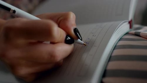 Woman's Hand Writing in Notebook with White Pen