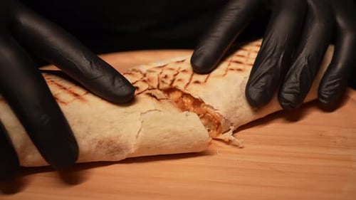 Hands Divide Tasty Wrapped Sandwich on Wooden Board