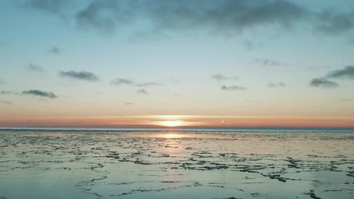 Drone flying over calm sea with melted ice at the surface at sunset, sunrise. Thick ice patterns vis