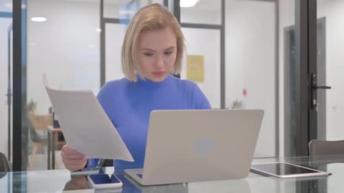 Young Woman Reviews Paperwork at Office Desk
