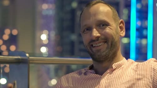 Smiling young man enjoys a relaxing evening on a city terrace alone at night