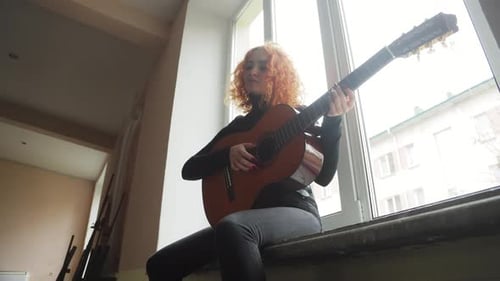 Woman Plays Guitar Sitting by Bright Window