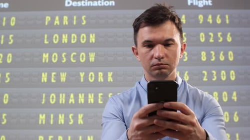 Man Standing in Front of an Airport Departure Board Checking Flight Information and Travel Updates