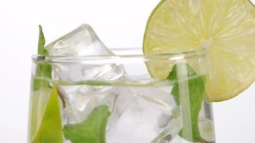 Close Up Of Ice Cube Falling In A Glass Of Fresh Lime And Mint Soda On The Light White Background