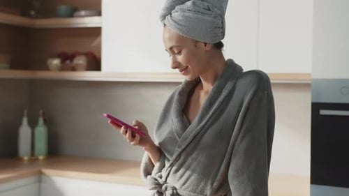 A Woman in a Bathrobe Interacts with Her Phone in a Cozy Kitchen